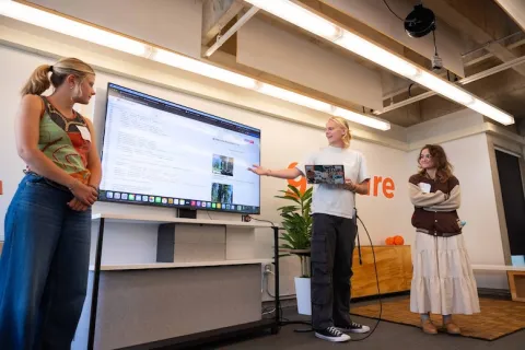 Three students presenting a topic at the front of a classroom.