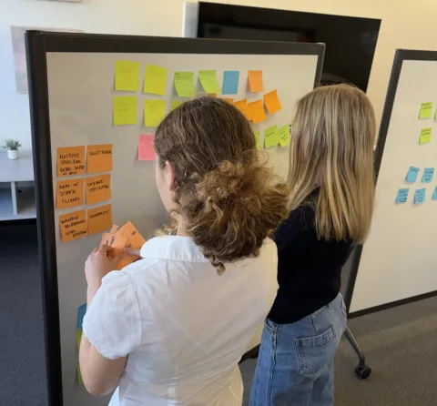 students at work, putting up sticky notes on a whiteboard